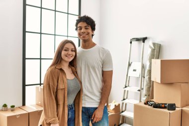 Genç çift mutlu bir şekilde gülümsüyor ve yeni evlerinde birbirlerine sarılıyorlar..