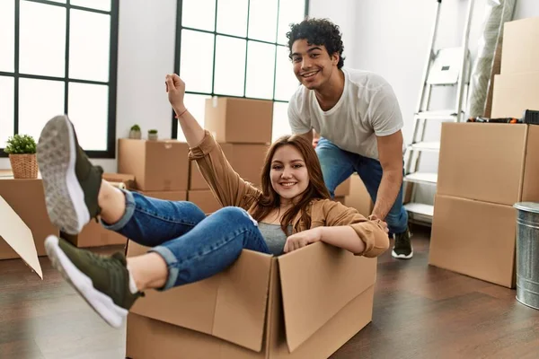 Young couple smiling happy playing with cardboard box as a car at new home.