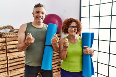 Orta yaşlı çift yoga minderi tutuyorlar. Elleriyle para hareketi yapıyorlar. Maaş istiyorlar. 