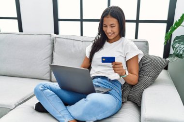 Evde kredi kartı tutan genç Latin kadın.