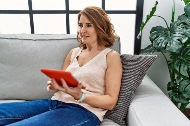 Orta yaşlı İspanyol kadın evde dokunmatik ped kullanarak gülümsüyor.