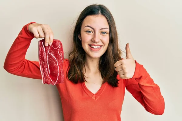 Joven Morena Sosteniendo Carne Cruda Sonriendo Feliz Positiva Pulgar Hacia —  Fotos de Stock