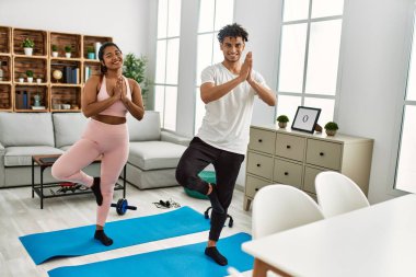 Gülümseyen genç Latin çift evde mutlu yoga pozu veriyor..