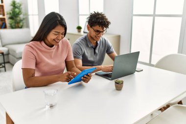 Genç latin çift evde masanın üzerinde dizüstü bilgisayar ve dokunmatik ped kullanarak çalışıyor..