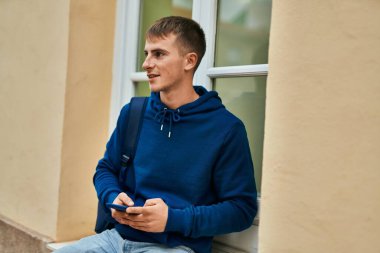 Üniversitede akıllı telefon kullanarak mutlu gülümseyen genç sarışın öğrenci..