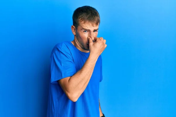 年轻的高加索人 穿着休闲的蓝色T恤 闻到一股难闻难闻的气味 用手指捂住鼻子呼吸 — 图库照片