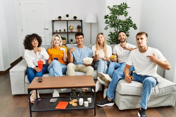 Bir grup insan evdeki koltukta oturmuş mutlu ve gururlu bir şekilde gülümseyen birini işaret ediyor. 