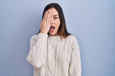 Mavi arka planda duran genç esmer kadın bir gözünü eliyle kapatıyor, yüzünde kendine güvenen bir gülümseme ve sürpriz bir duygu var.. 