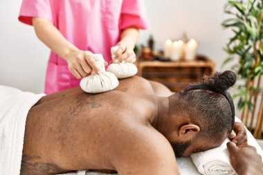 Genç Afrikalı Amerikalı adam güzellik merkezinde Tayland çantalarıyla sırt masajı yaptırıyor.