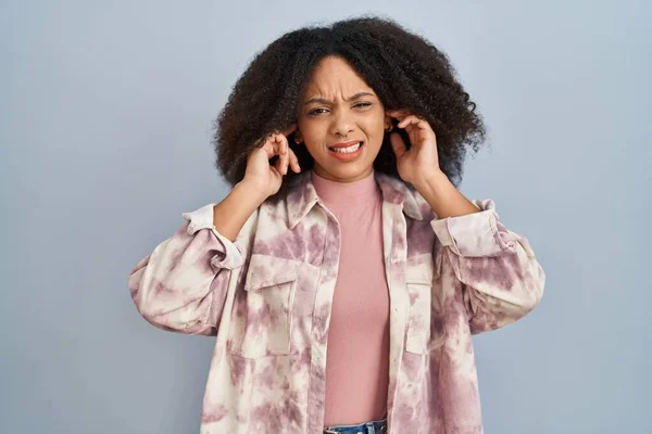 若いアフリカ系アメリカ人の女性は 大きな音楽のノイズに悩まされた表情で指で耳を覆う青い背景に立っています 聴覚障害の概念 — ストック写真
