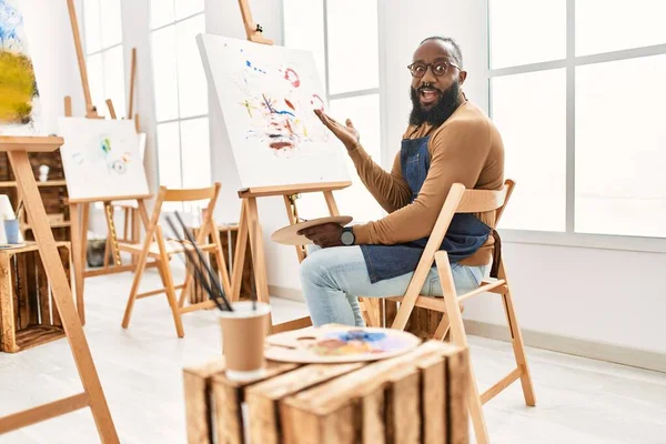 アフリカ系アメリカ人アーティストの男性が笑顔で勝利を祝うアートスタジオでキャンバスに絵を描き 手を上げて勝者の表情 — ストック写真