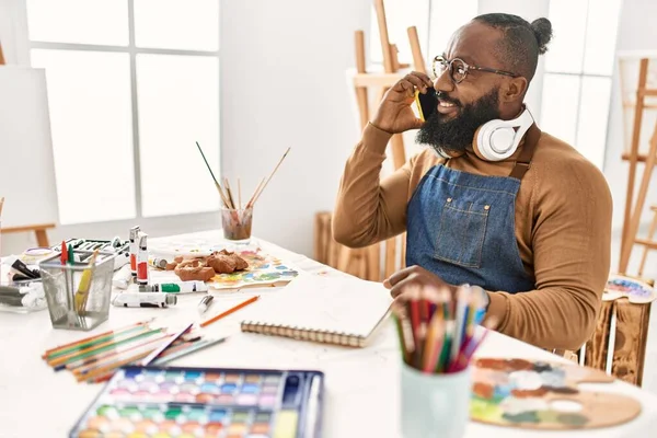 若いアフリカ系アメリカ人のアーティストがヘッドフォンを使用してアートスタジオでスマートフォンで話しています — ストック写真