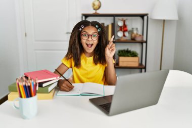 Genç Afro-Amerikan kız ödevini evde yapıyor ve başarılı bir fikirle işaret ediyor. Heyecanlı ve mutlu. Bir numara.. 