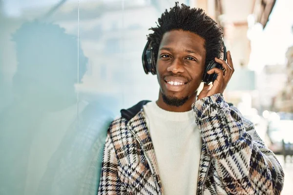 Handsome black man with afro hair wearing headphones smiling happy outdoors