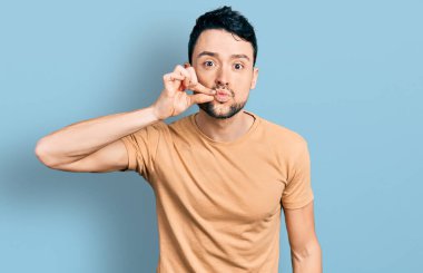 Sakallı, sıradan tişört giyen ağzı ve dudakları parmaklarıyla kapanan İspanyol bir adam. gizli ve sessiz, tabu konuşması 