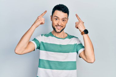 Gündelik kıyafetler giyen genç İspanyol adam gülümseyerek iki eliyle kafasını işaret ediyor. Harika bir fikir ya da düşünce, iyi bir hafıza. 