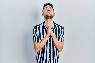 Gündelik giysiler giyen genç İspanyol adam elleri bağlı yalvarıyor ve dua ediyor. Yüzünde umut ifadesi var. Çok duygusal ve endişeli. Yalvarıyor. 