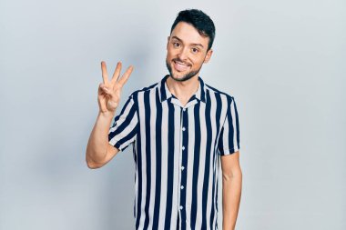 Gündelik kıyafetler giyen genç İspanyol adam üç numarayı gösterip işaret ederken kendinden emin ve mutlu gülümsüyor.. 