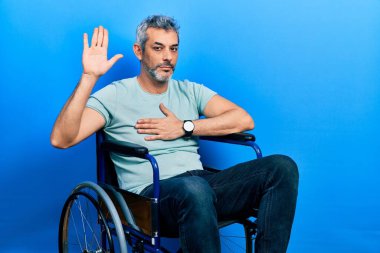 Yakışıklı, orta yaşlı, gri saçlı, tekerlekli sandalyede oturan, eli göğsünde ve avuç içi açık yemin eden, sadakat yemini eden bir adam. 