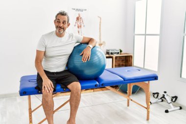 Orta yaşlı İspanyol bir adam ağrı kesici kliniğinde pilates topu tutuyor gülümsüyor ve başka tarafa bakıyor.. 