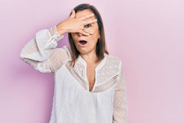 Orta yaşlı İspanyol kadın gündelik giysiler giymiş. Şoka girmiş. Yüzü ve gözlerini kapamış, utanmış ifadesiyle parmaklarından bakıyor.. 