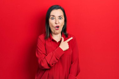 Orta yaşlı, gündelik kıyafetler giyen İspanyol bir kadın parmaklarıyla yüzünü göstererek şaşırdı, ağzı açık hayret içinde kaldı.. 