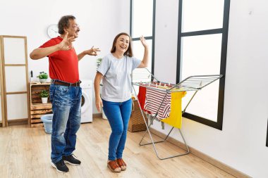 Orta yaşlı erkek ve kadın çamaşırhanede çamaşır makinesini beklerken dans ediyorlar.