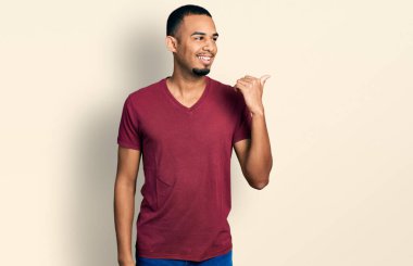 Young african american man wearing casual t shirt pointing thumb up to the side smiling happy with open mouth 