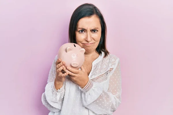 Middle Age Hispanic Woman Holding Piggy Bank Skeptic Nervous Frowning — 스톡 사진