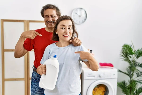 Średniego Wieku Międzyrasowa Para Robi Pranie Trzymając Butelkę Detergentu Wskazując — Zdjęcie stockowe