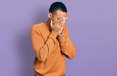 Genç, Afro-Amerikan bir adam, günlük kıyafetler giyiyor ve ağlarken suratını ellerle kapatıyor. depresyon kavramı. 
