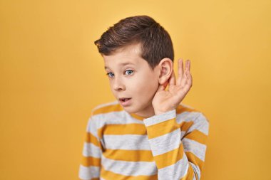 Sarı arka planda dikilen beyaz bir çocuk kulağından kulaklarına gülümseyerek dedikodulara ve dedikodulara kulak veriyor. Sağırlık kavramı. 