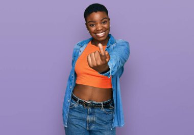 Genç Afro-Amerikan kadın gündelik giysiler giyip, el kol hareketi yaparak, mutlu ve gülümseyen insanları davet ediyor. 