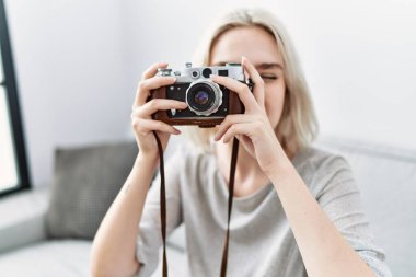 Beyaz bir kadın evde kamerayla gülümsüyor.