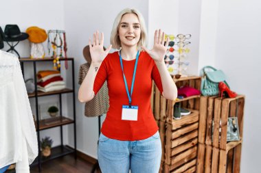 Perakende mağazasında yönetici olarak çalışan genç beyaz kadın on numarayı gösterip işaret ederken kendinden emin ve mutlu bir şekilde gülümsüyor.. 