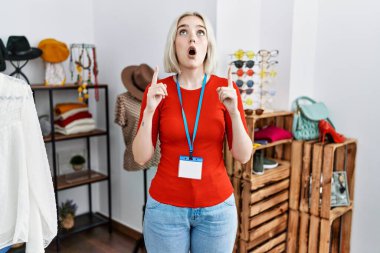 Perakende mağazasında yönetici olarak çalışan genç beyaz kadın şaşkın ve şaşırmış bir şekilde yukarı bakıyor ve parmaklarıyla işaret ediyor ve kollarını kaldırıyordu.. 