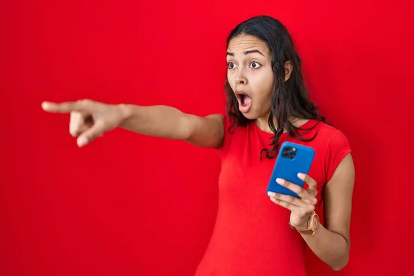 Junge Brasilianerin Mit Smartphone Über Rotem Hintergrund Zeigt Mit Dem — Stockfoto