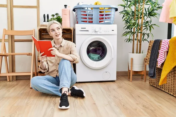 Young Caucasian Woman Reading Book Waiting Washing Machine Laundry Room — стоковое фото