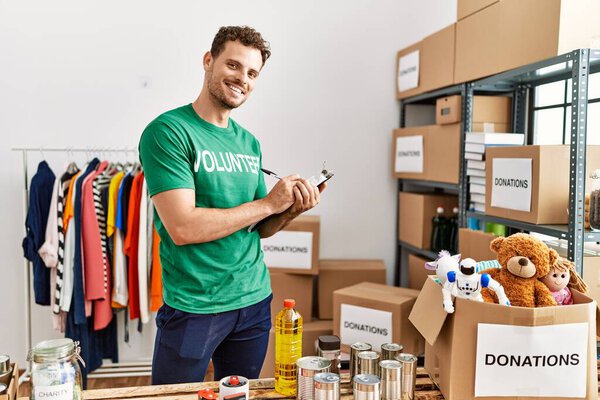 Молодой латиноамериканец, одетый в форму добровольца, пишет в блокноте благотворительного центра