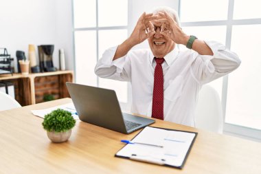 Ofiste çalışan kıdemli bir adam bilgisayarla çalışıyor. Dürbün gibi hareket ediyor, gözleri parmaklarından bakıyor. çılgın ifade. 