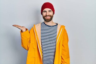 Sarı yağmurluk giyen, gülümseyen, eli avucunda kameraya bakan beyaz bir adam.. 