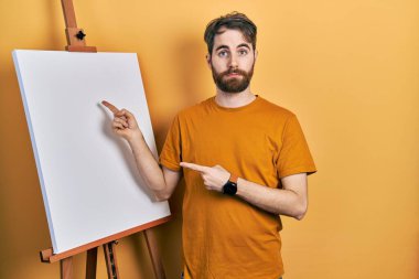 Ressam sehpasına işaret eden beyaz sakallı bir adam depresyonda ve üzüntüden ağlıyor, ağlıyor ve korkuyor. hüzünlü ifade. 