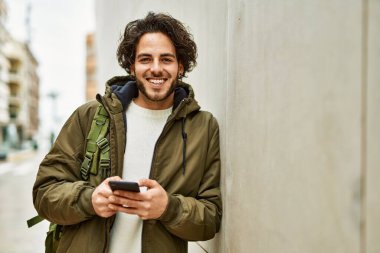 Duvara dayanmış akıllı telefon kullanan yakışıklı İspanyol.
