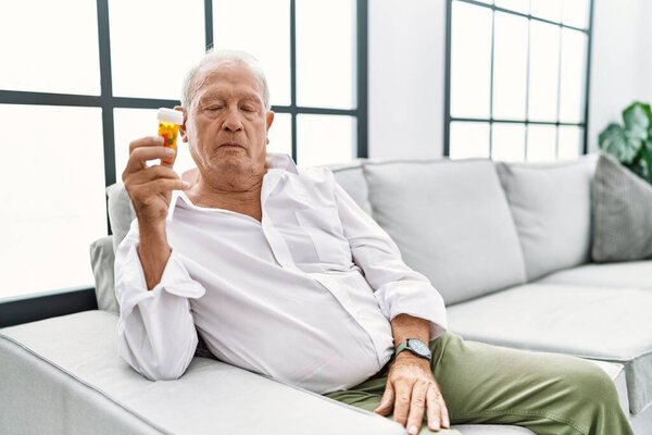 Senior man holding pills relaxed with serious expression on face. simple and natural looking at the camera. 