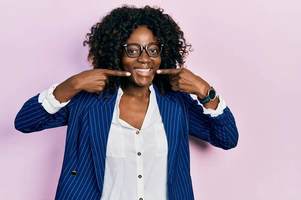 若いアフリカ系アメリカ人の女性は ビジネス用の服や眼鏡を身に着けて 明るい表情と指の歯と口で指して笑っています 歯の健康の概念 — ストック写真