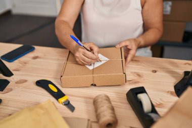 Orta yaşlı kadın ecommerce iş işçisi ofiste paket üzerine yazıyor.