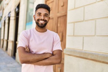 Yakışıklı İspanyol adam dışarıda kollarını kavuşturarak mutlu gülümsüyor. Sokakta gülen yüzlü, arkadaş canlısı bir genç..