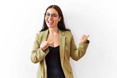 Genç esmer kadın izole edilmiş arka planda duruyor. Arka tarafı işaret ediyor. Baş parmakları havada, kendinden emin gülümsüyor. 