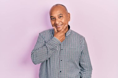 Orta yaşlı, sıradan kıyafetler giyen, kameraya kendinden emin bakan kolları çapraz ve çenesi havada gülümseyen Latin bir adam. Olumlu düşünmek. 