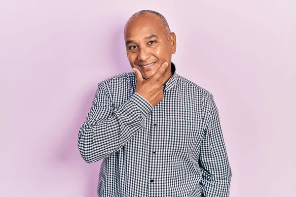 Orta yaşlı, sıradan kıyafetler giyen, kameraya kendinden emin bakan kolları çapraz ve çenesi havada gülümseyen Latin bir adam. Olumlu düşünmek. 